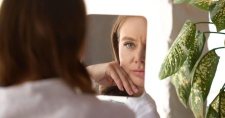 Frau betrachtet ihre Haut im Spiegel – erste Anzeichen von Hautalterung