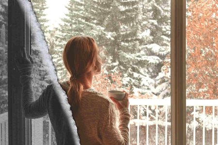 Stiller Brand: Wenn Entzündung Energie frisst Frau blickt im Winter aus dem Fenster – Sinnbild für stille chronische Entzündungen im Körper