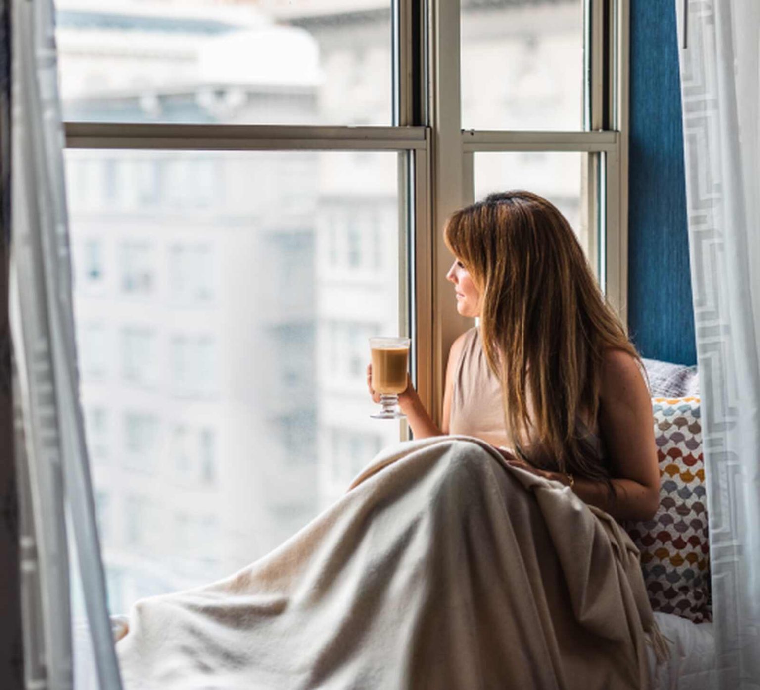 Frau sitzt morgens am Fenster und blickt nachdenklich ins Licht – Sinnbild für nachlassende Energie und Regeneration