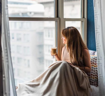 Frau sitzt morgens am Fenster und blickt nachdenklich ins Licht – Sinnbild für nachlassende Energie und Regeneration