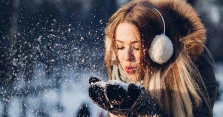 Frau im Winter bläst Schnee aus den Händen – Symbolbild für Kälte, Stress und Immunsystem im Winter