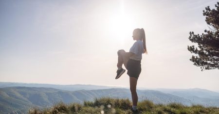 Frau dehnt ihr Knie auf einem Berggipfel – Symbol für gesunde und bewegliche Gelenke